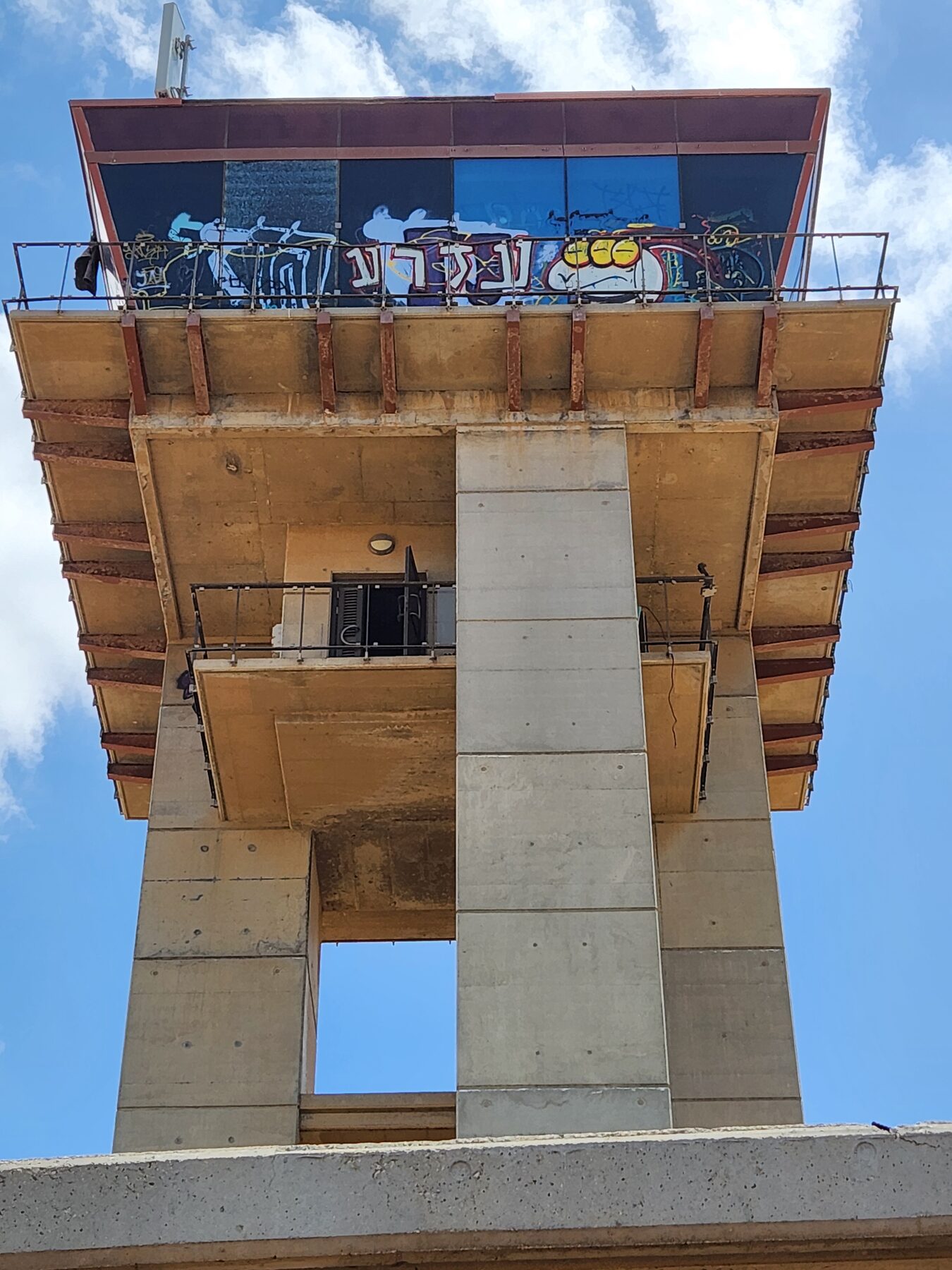 The Sde Dov control tower seen from below, its glazed cabin covered in graffiti