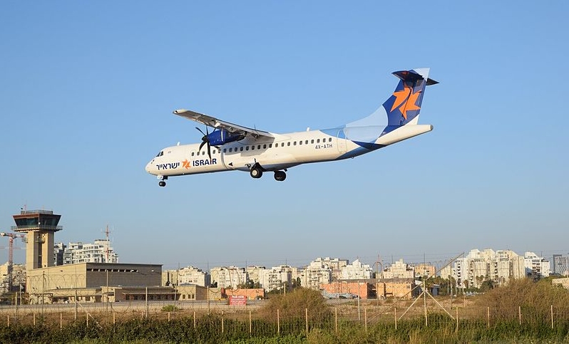 An Israir turboprop on final approach at Sde Dov with the control tower and city skyline behind
